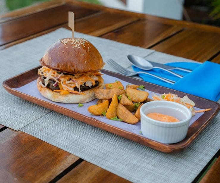 Burger with slaw and potato wedges on a wooden tray