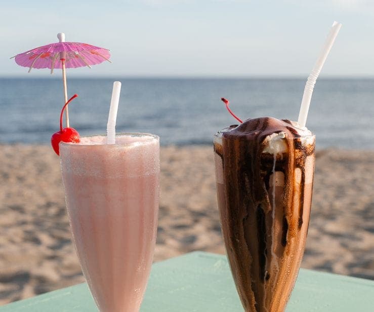 Two milkshakes with cherries on a pastel table by the sea